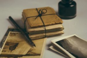 A fountain pen lying next to old black and white photographs and a bundle of documents wrapped in brown paper and tied up with black string