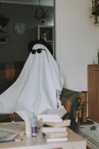 person wearing a white sheet over their body and sitting on a couch. they are also wearing sunglasses and a hat.