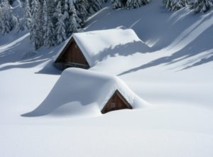 two wooden cottages almost totally covered in snow 