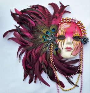 A pink mardi gras mask with purple, blue, and yellow feathers sticking out of it.