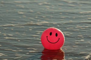 A red ball with a smiley face on it. The ball is floating in a large body of water. 