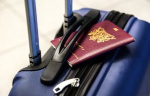 A red passport tucked into the handle of a blue wheeled suitcase 