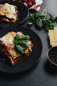 Lasagna on black plate with a sprig of a green plant on the food.