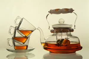 Three clear glass teacups stacked on top of each other. Each one contains a small amount of tea, and they're sitting next to a clear glass teapot that is half full of tea.