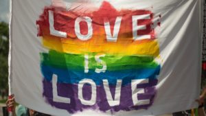 White piece of cloth that has a rainbow and the phrase "love is love" painted on it. 