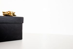 A black gift box with a gold bow on it. 