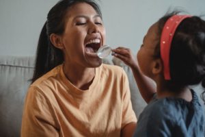 Child looking into a woman's mouth with a magnifying glass 