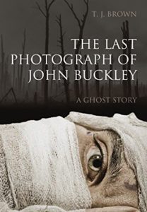 The Last Photograph of John Buckley by T.J. Brown book cover. Image on cover shows a man’s bandaged face as he’s lying down. Only his eyes are visible. 