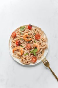 A plate filled with pasta, shrimp, and cooked tomatoes.