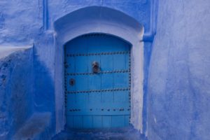 A small, locked blue door in the side of a large blue building.