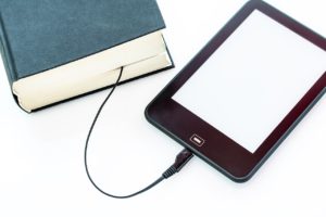 An ereader with it’s cord tucked between the pages of a hardcover book. 