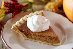 Close-up photo of a slice of pumpkin pie with a dollop of whipped cream on it. The pie is sitting on a white dinner plate. 