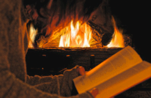 Person reading a book while sitting next to a crackling fireplace. 