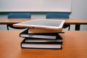 An e-reader lying on top a stack of hardback novels.