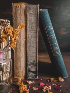 Photo of antique books standing next to a vase filled with dry flowers. 