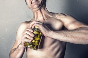 Man struggling to open a jar of pickles. The man is not wearing a shirt. 