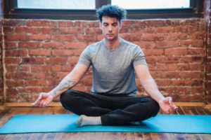 Man meditating while sitting on a blue yoga mat 