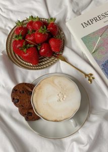 Strawberries, coffee, cookies, and an art book on a white sheet. 