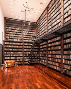 A large, airy library filled with two stories worth of books. There is an orange chair next to a window in the corner. 