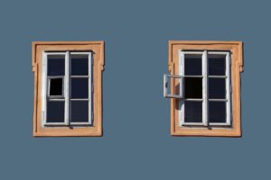 Two identical windows in the side of a building. Each window is comprised of eight small panes. The bottom left pane of glass on the right window is opened. All others are closed. 