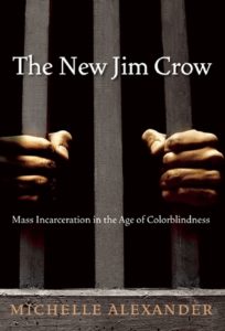 The New Jim Crow: Mass Incarceration in the Age of Colorblindness by Michelle Alexander book cover. Image on cover shows the hands of a black man who is gripping rails in a prison cell. His face is not visible. 