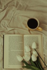 Coffee, tulips, and an opened hardback book lying on a white bedsheet. 