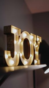 A sign shaped like the word “Joy.” It is covered in about 16 glowing white lights. 