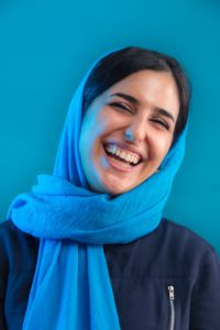 A woman with black hair who is wearing a blue scarf and a blue shirt. She is laughing and looks perfectly joyful. 