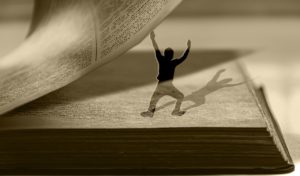 Silhouette of 3-inch tall person holding up the page of a book.