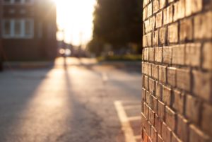 An empty city street that has warm sunlight streaming down onto it and the brick wall of a building on it.
