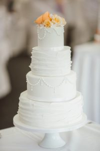 A four-tier white wedding cake with orange flowers on the top of it. 