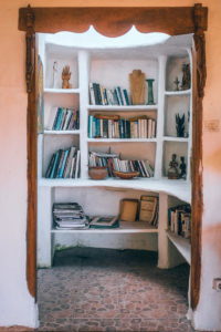 A nook in a house that contains a while bookshelf built into the wall. The doorway has a nice wooden frame with some leaves carved into it. 