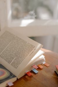 Coloured tabs of paper sticking out of a book that’s opened and lying on a wooden table. 