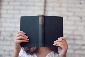 Woman holding antique book with blue cover in front of her face. 