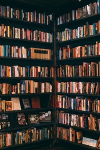 A photo of two bookcases next to each other, each covering one wall in a room and gently touching in the corner. They are both filled with books. 