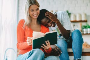 Two women laughing while reading a book together. 