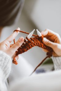 A person wearing a white sweater who is beginning to knit something with dark red yarn. 