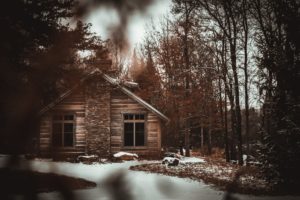 A quiet wooden cabin in a snowy winter woods. The cabin has a stone chimney. 