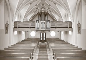 An empty church that has white wooden pews and white painted statues of saints on their walls. 