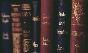 Leather-bound copies of several classic novels that are sitting on a bookshelf. The one with the clearest title has a navy blue cover and says “Pride and Prejudice” with the name Jane below it. You cannot see her last name. 
