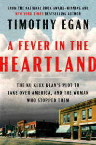 Book cover for A Fever in the Heartland: The Ku Klux Klan's Plot to Take Over America, and the Woman Who Stopped Them by Timothy Egan. Image on cover shows a photograph of a small town street that has stores on the ground level and apartments on the second level. The sky is dark and ominously cloudy in places with blue skies at the very top of the cover. There are a few scattered cars on the street. 