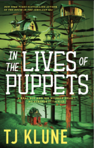 Book cover for In the Lives of Puppets  by T.J. Klune. Image on the cover is a drawing of a little red cottage in a forest filled with wooden tree-like items that have no leaves and oddly smooth trunks. Maybe they’re made out of metal and only look like wood? The three “tree” structures closest to the red cabin have little houses of their own installed high up on their branches hundreds of feet up in the air. One little house is yellow and round. The second is comprised of metal and has a roof that slopes over the sides of the house so that the walls can’t even hardly be seen. It has a solar panel on top of it. The third house is clear and seems to be made of glass. There are thin wires connecting all three houses, possibly to share electricity. 