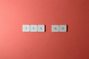 A photo of scrabble tiles against a salmon background. The tiles have been arranged to spell out the words “yes” and “no.”