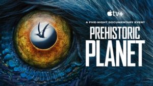 Poster for season two of the documentary Prehistoric Planet. It shows a close-up drwaing of a dinosaur’s eye. The dinosaur has blue feathers and a yellow-brown iris. You can see the reflection of a flying dinosaur in this dinosaur’s eye which is cool.