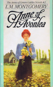 Book cover for Anne of Avonlea by L.M. Montgomery. Image on cover is a drawing of Anne as a young woman whose hair is tied up into a bow. She’s standing outdoors and gathering yellow flowers on a spring day. 