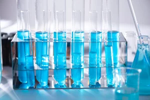 Mysterious blue liquid in a beaker, a pipette, and a series of glass test tubes that are lined up neatly in a row. 