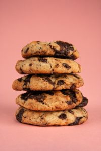 Closeup shot of five chocolate chip cookies that have been stacked on top of each other against a peach-coloured background. 