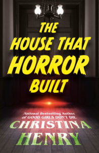 Book cover for https://www.goodreads.com/book/show/196834746-the-house-that-horror-built. Image on cover shows an eerie red glowing light that looks like an alien spaceship hanging low over the floor in an otherwise almost pitch black room. You can see two white lightbulbs above it and the dim outline of a large wooden door, but the rest of the room is shrouded in darkness. 