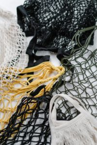 Closeup of eco-friendly mesh bags. Two are black, two are white, and one is yellow. They are all arranged in a circle against a white background. 