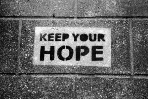 The phrase “keep your hope” has been spray painted onto the sidewalk in this black-and-white photo.